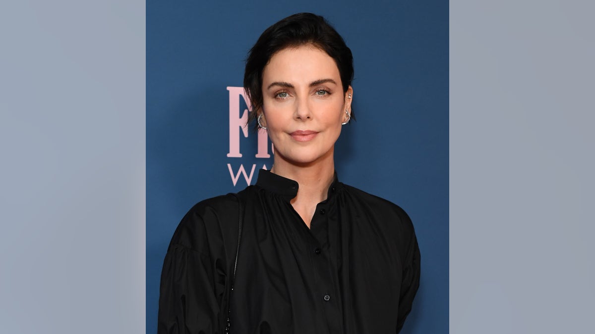 Charlize Theron with dark hair in a black shirt.