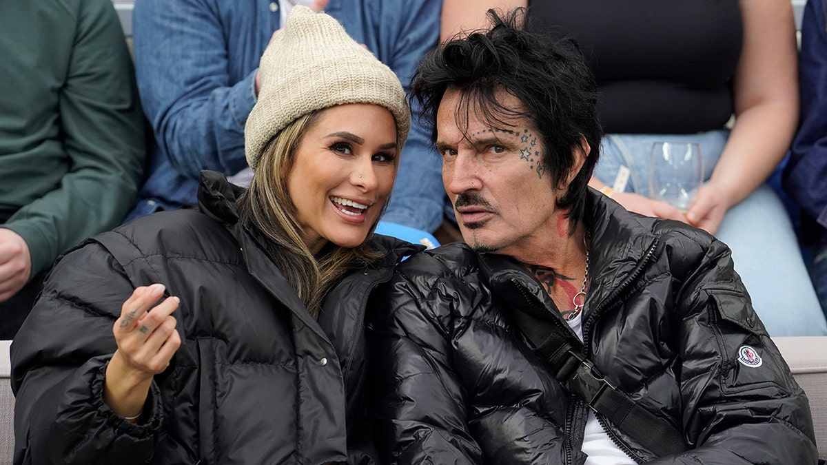 Brittany Furlan wears a beanie and black jacket while chatting with her husband Tommy Lee also in a black jacket at SoFi Stadium