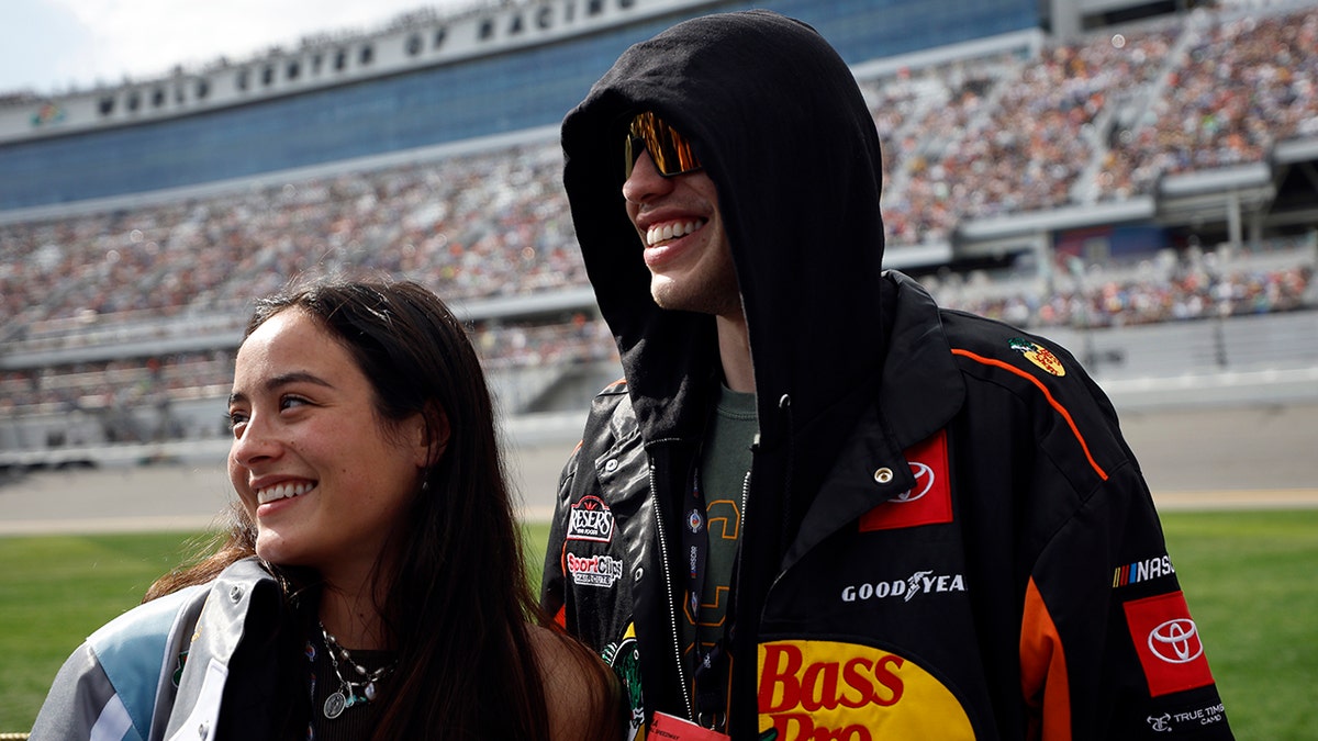 Pete Davidson in a black sweatshirt with logos smiles with girlfriend Chase Sui Wonders in Daytona Beach Florida for the NASCAR Cup Series