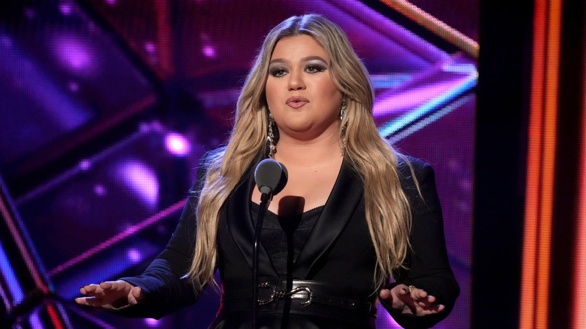 Kelly Clarkson in a black outfit behind a microphone at the iHeartRadio Music Awards