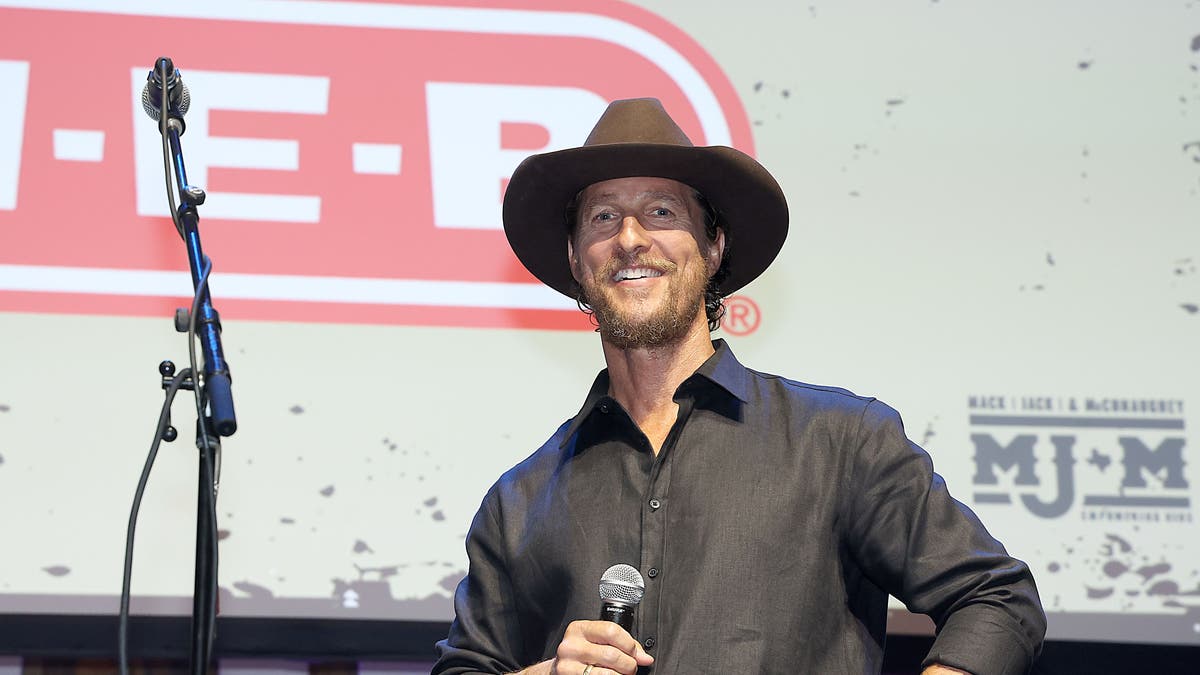 Matthew McConaughey on stage wearing a cowboy hat and holding a microphone