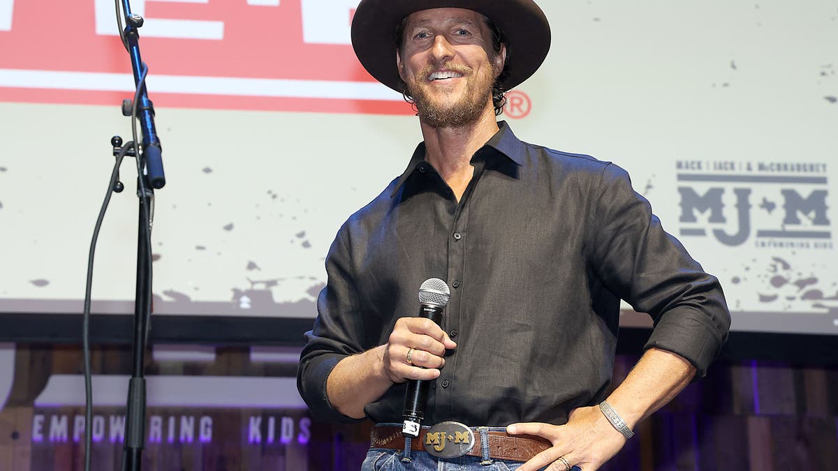 Matthew McConaughey on stage wearing a cowboy hat and holding a microphone