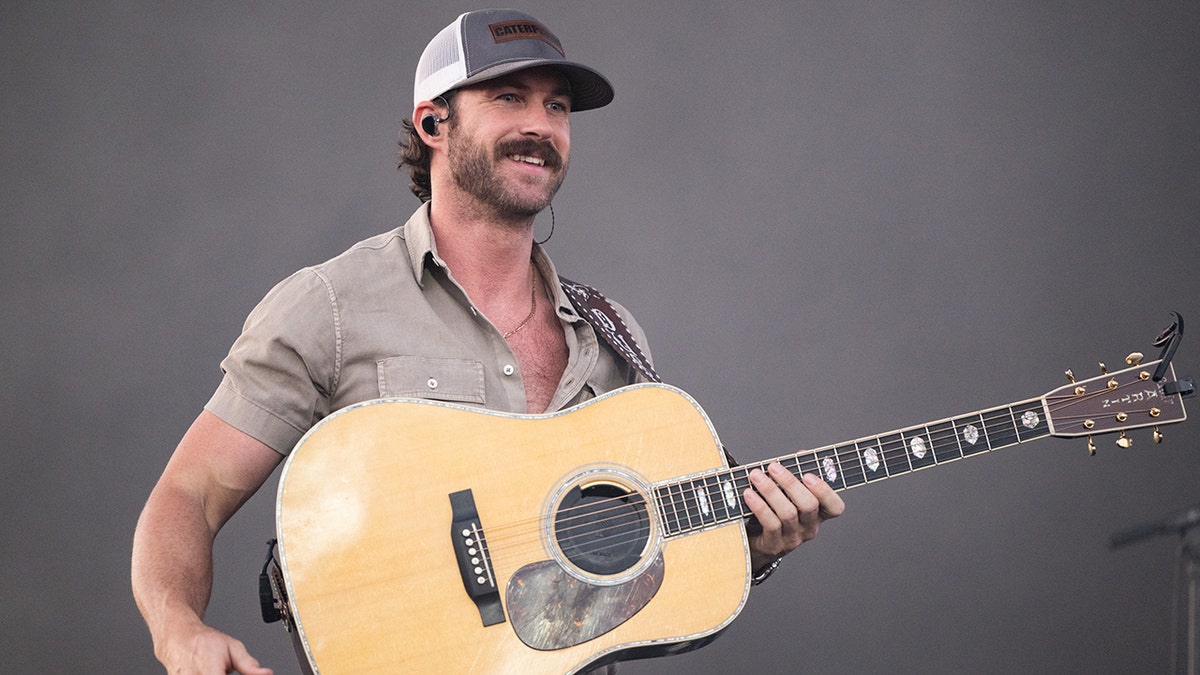 Riley Green holds a guitar and performs on stage at Stagecoach wearing a hat