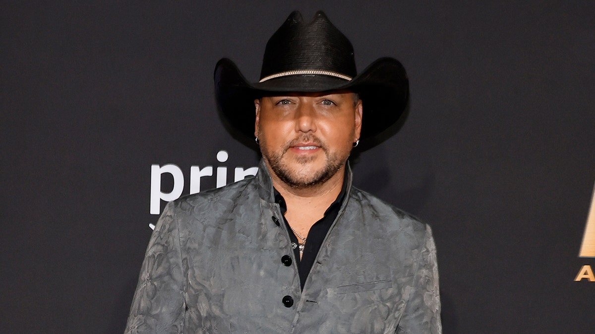 Jason Aldean smiles on the carpet in a black cowboy hat