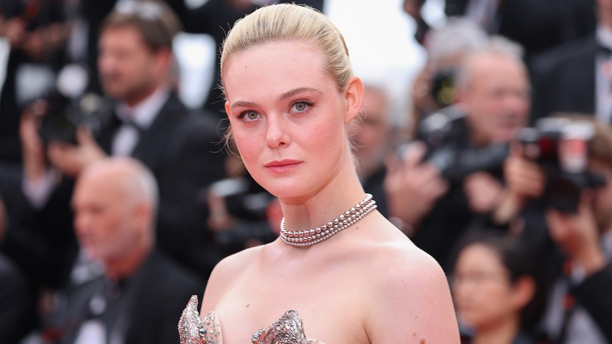 Elle Fanning smizes on the red carpet in Cannes wearing a strapless dress and a chain necklace