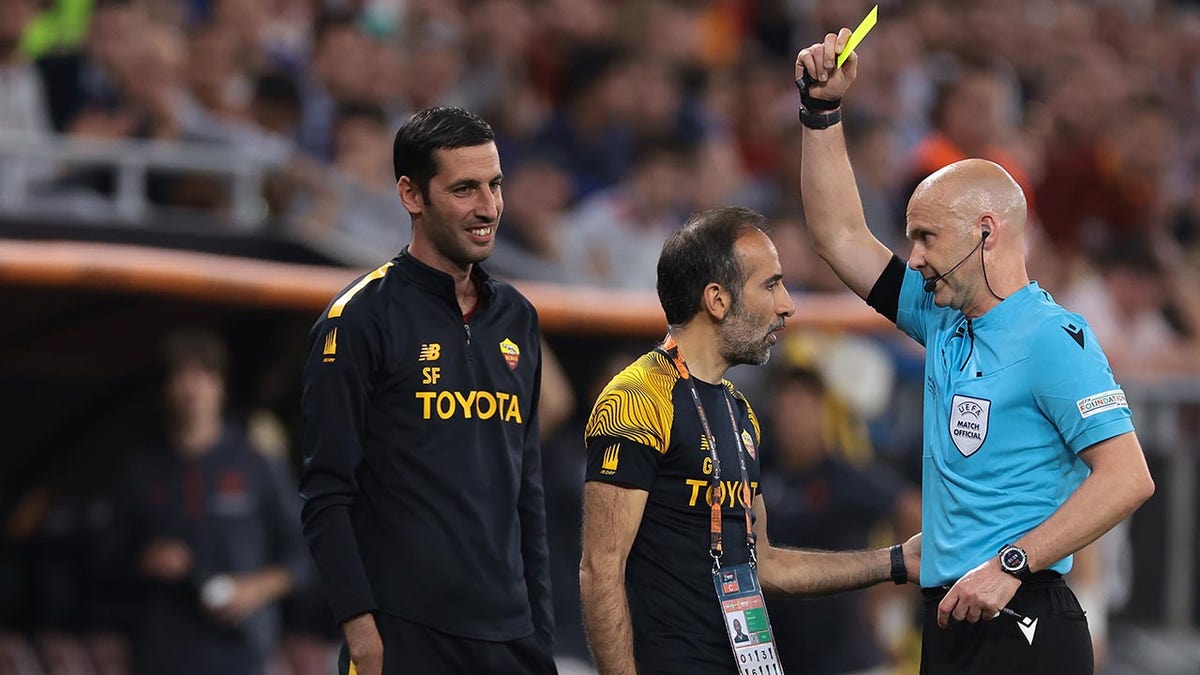 Anthony Taylor issues a yellow card to a Roma coach
