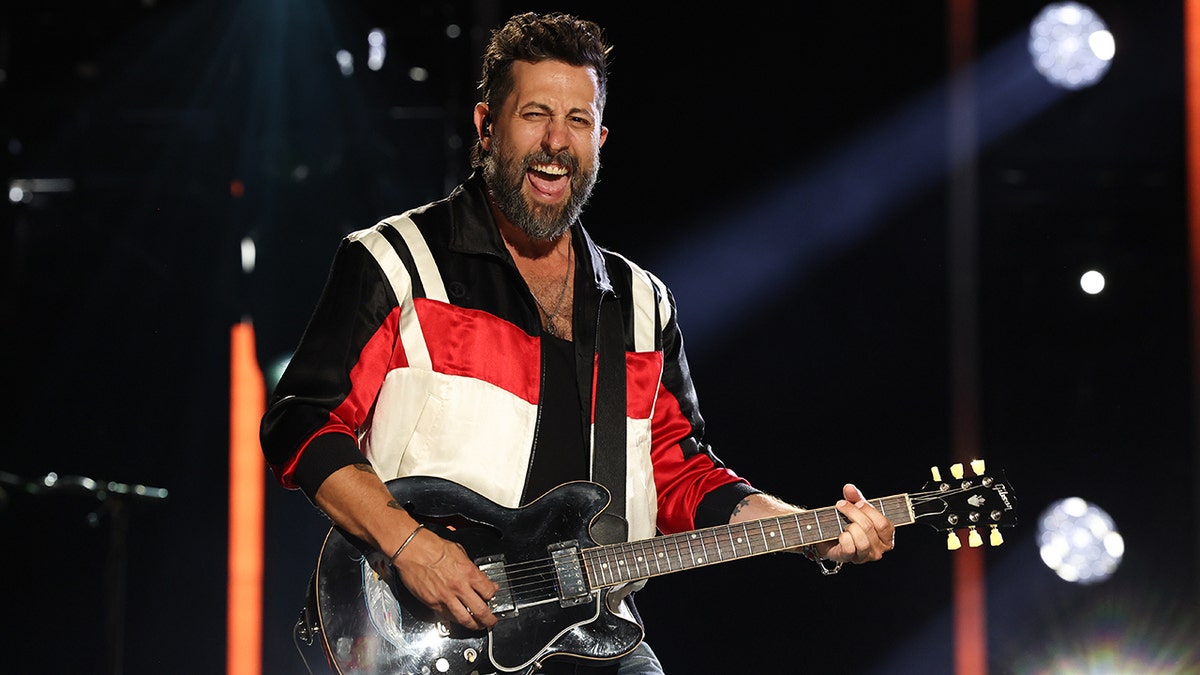 Matthew Ramsey strums the guitar in a black/red/white jacket while performing at CMA Fest with Old Dominion