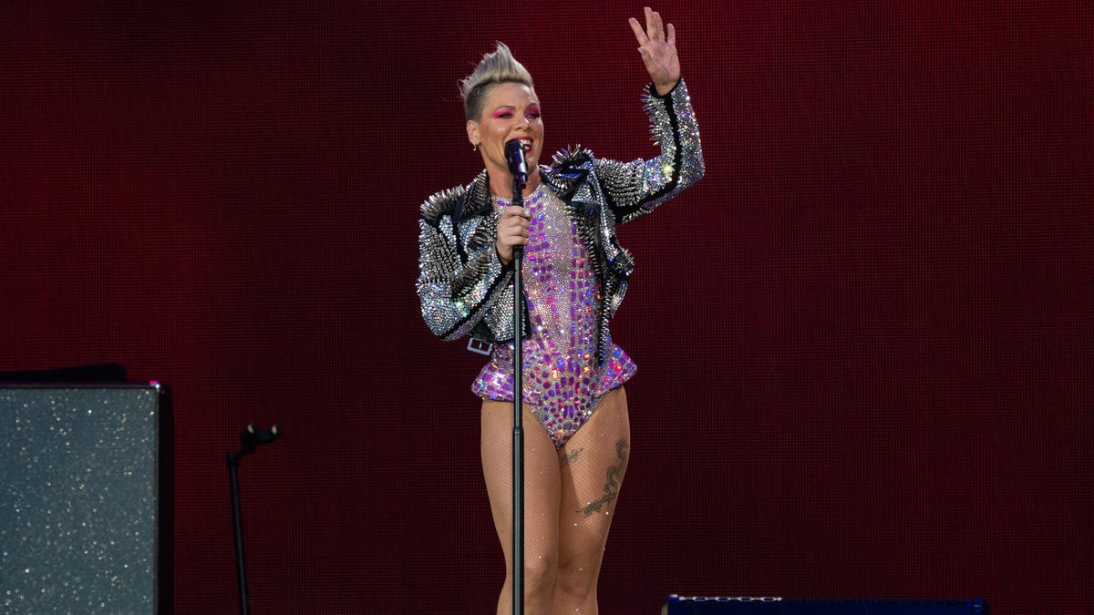 Pink in a purple sparkly bodysuit and silver jacket waves to fans while on stage in London