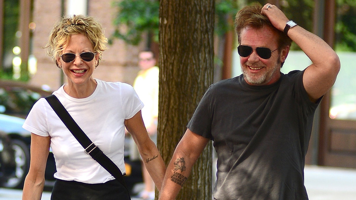 Meg Ryan in a white t-shirt laughs while holding hands with John Mellencamp on the streets of New York City
