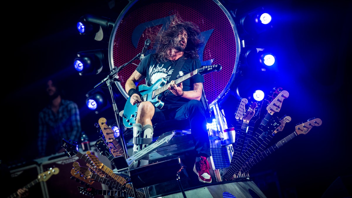 Dave Grohl sitting on his throne onstage rocking out with a guitar with his leg in a boot