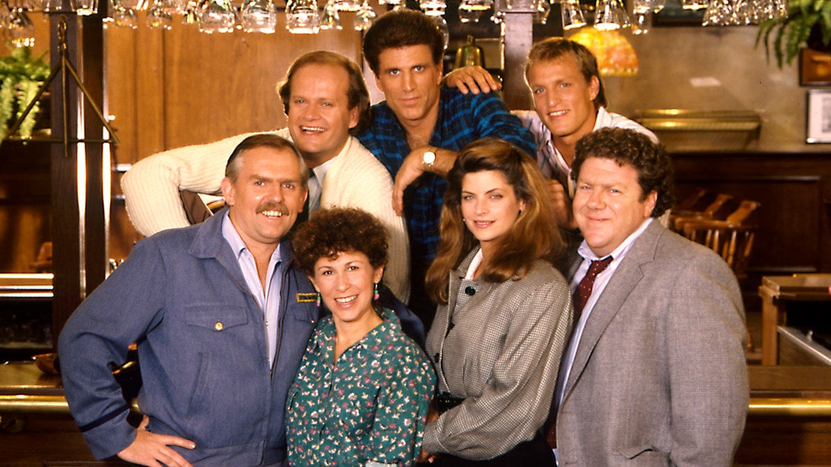 The cast of 'Cheers' smiles in a photo, including Kirstie Alley, Woody Harrelson, Ted Danson, Kelsey Grammer