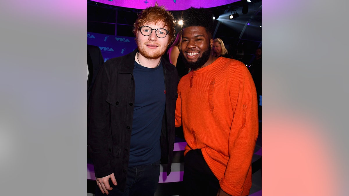 Ed Sheeran soft smiles wearing glasses for a photo with Khalid in red at the MTV Video Music Awards