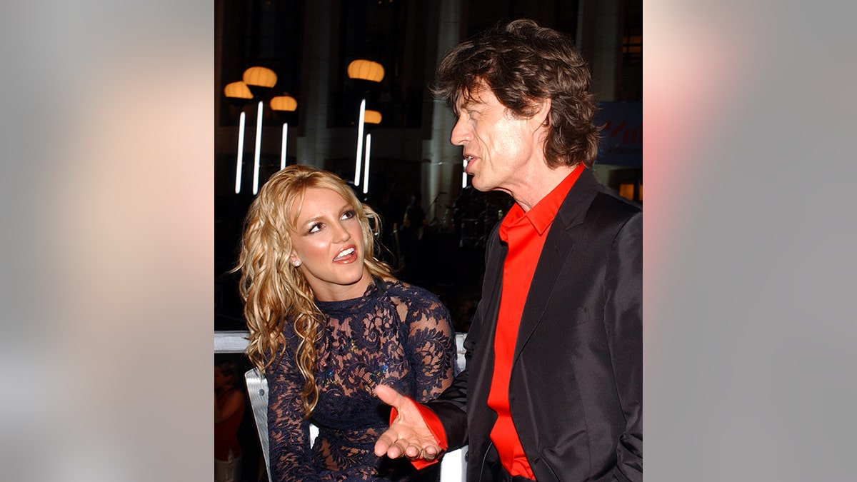 Britney Spears looks hilariously at Mick Jagger as he speaks during an interview at the 2001 VMAs