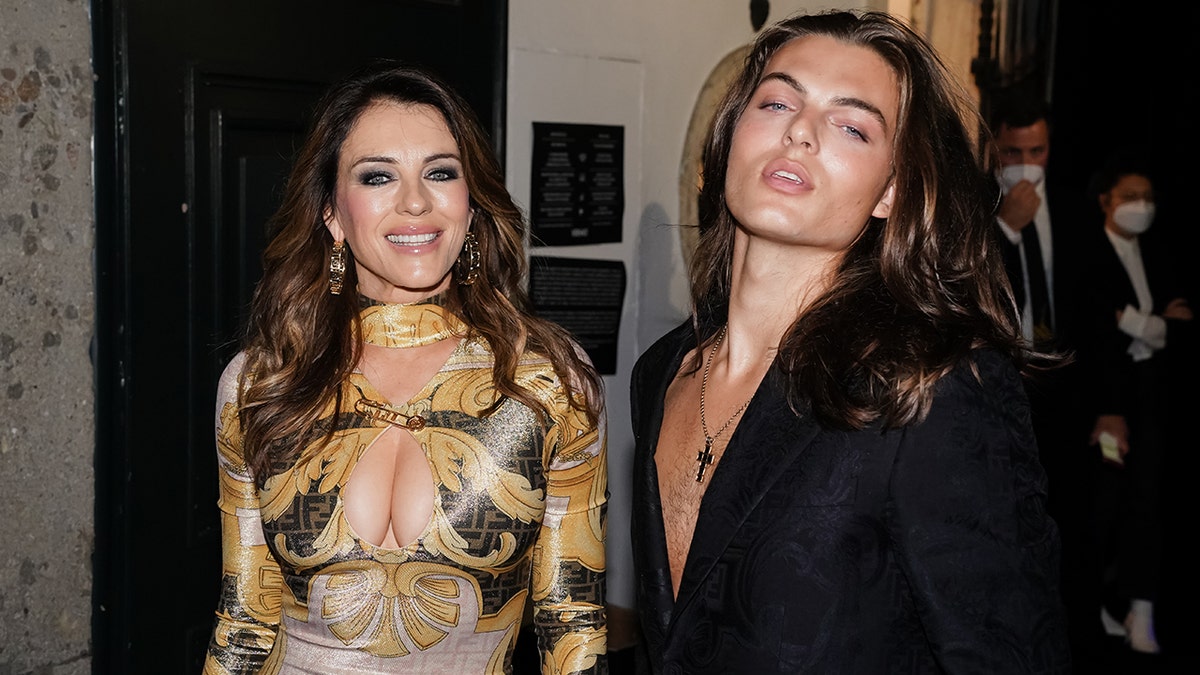 Elizabeth Hurley wearing a golden Versace dress next to her son Damian Hurley wearing a black suit
