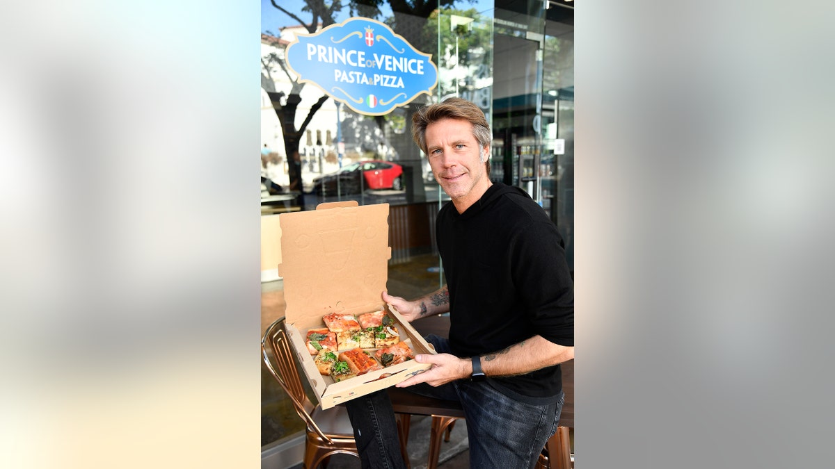 Emanuele Filiberto holding a box of pizza wearing a black sweater