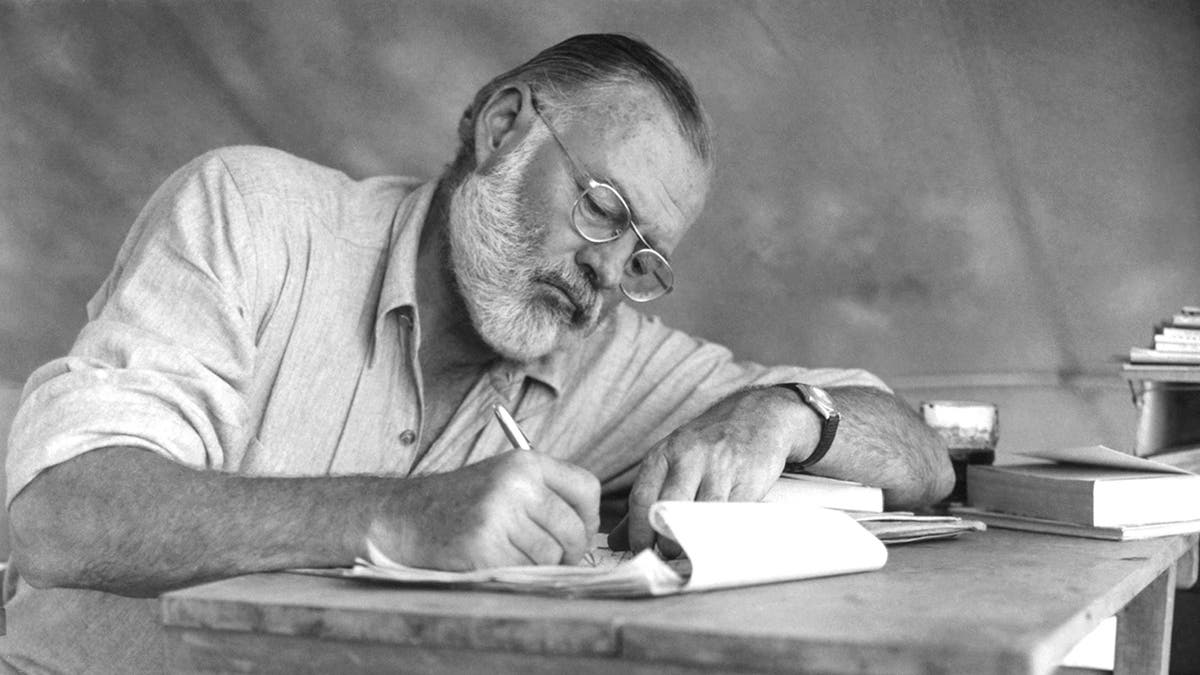 Ernest Hemingway writing on a notebook pad with a pen