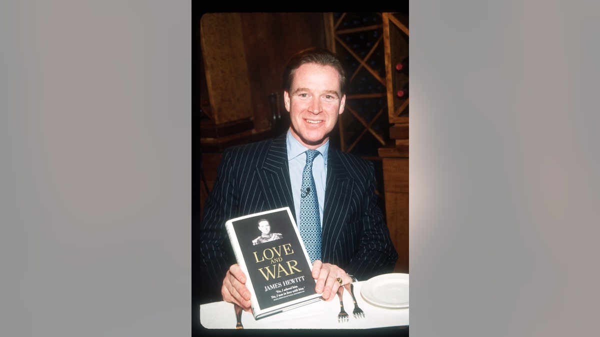 James Hewitt in a dark suit and blue shirt with blue tie holding a book