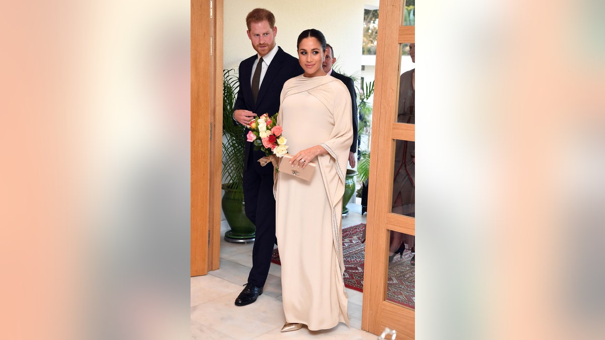Meghan Markle wearing a creme floor length dress while wearing flowers