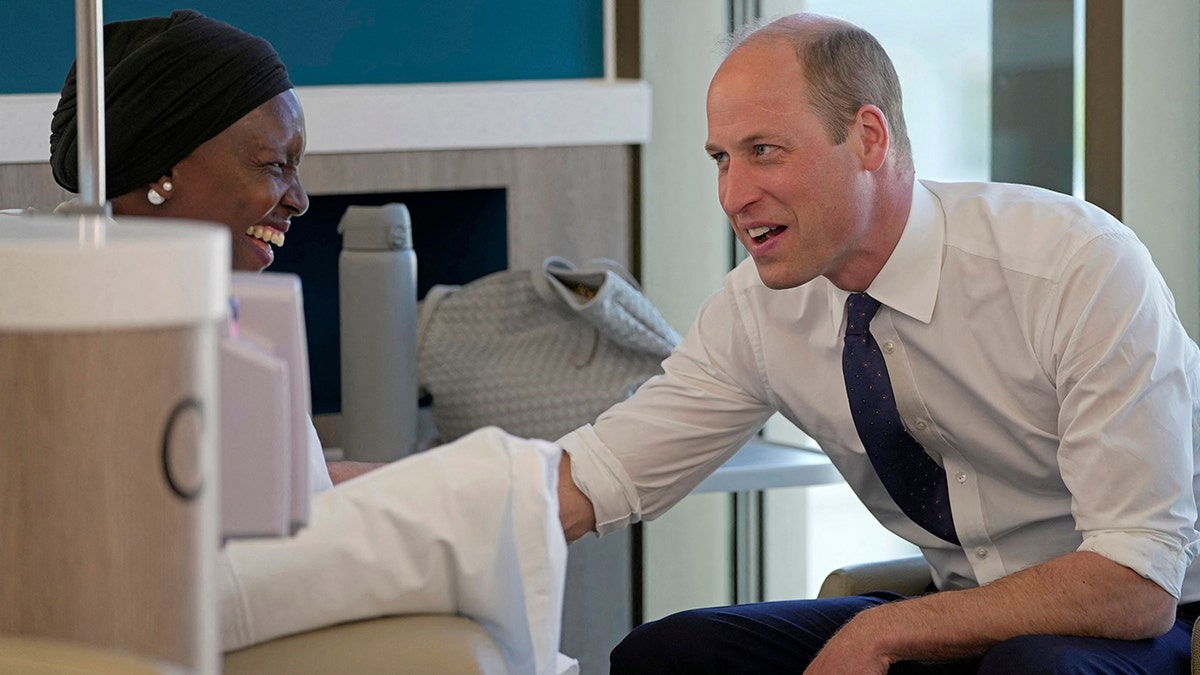 Prince William in a rolled up white shirt and tie speaking to a woman wearing a white outfit
