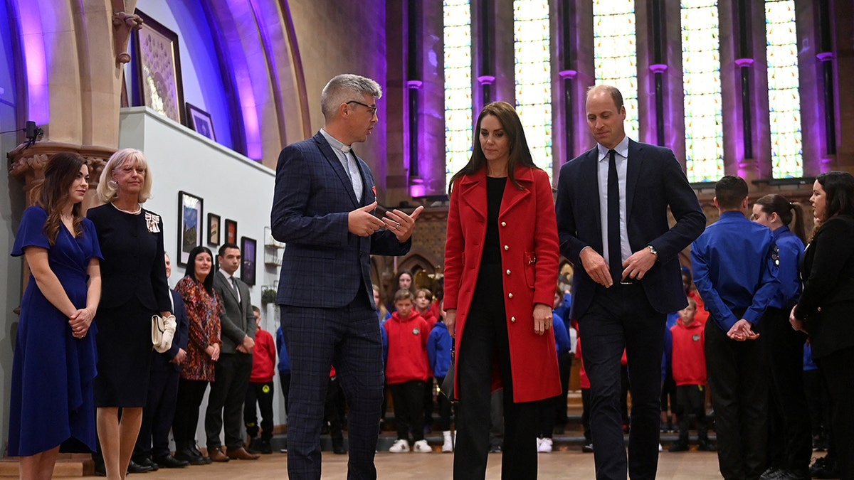 Prince William wearing a blue suit and Kate Middleton wearing a red coat inside St. Thomas Church