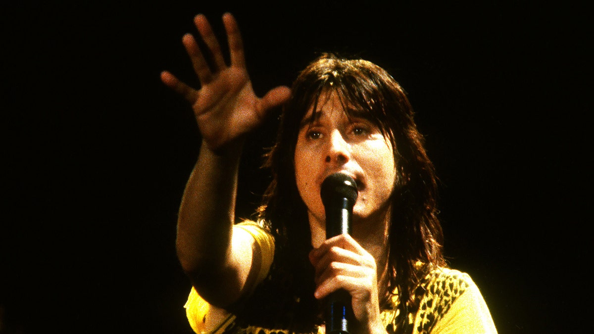 Steve Perry wearing a yellow shirt and singing on a mic