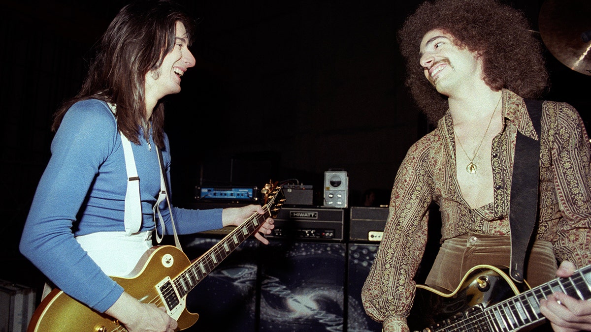 Steve Perry and Neal Schon playing guitar to each other and smiling