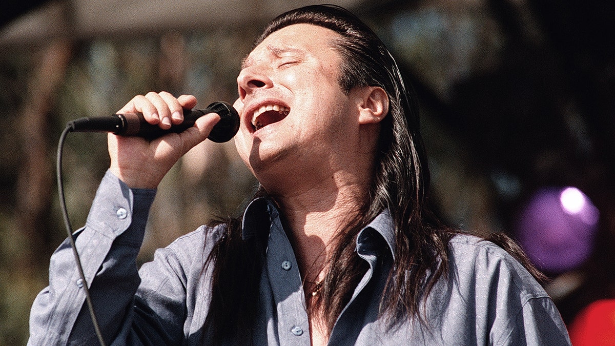 A close-up of Steve Perry singing wearing a blue shirt