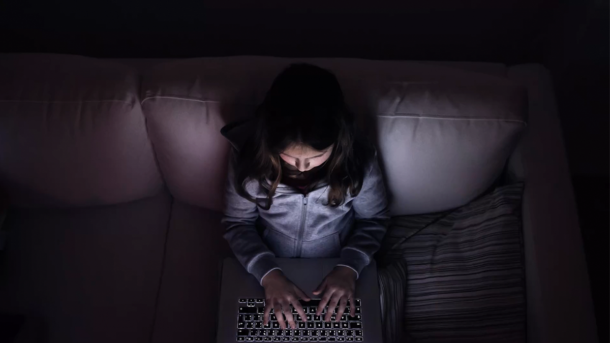 Little girl, sitting in a dark, playing with laptop .