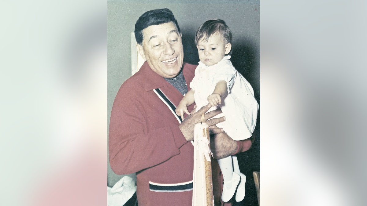 Louis Prima wearing a red sweater holding his daughter Lena