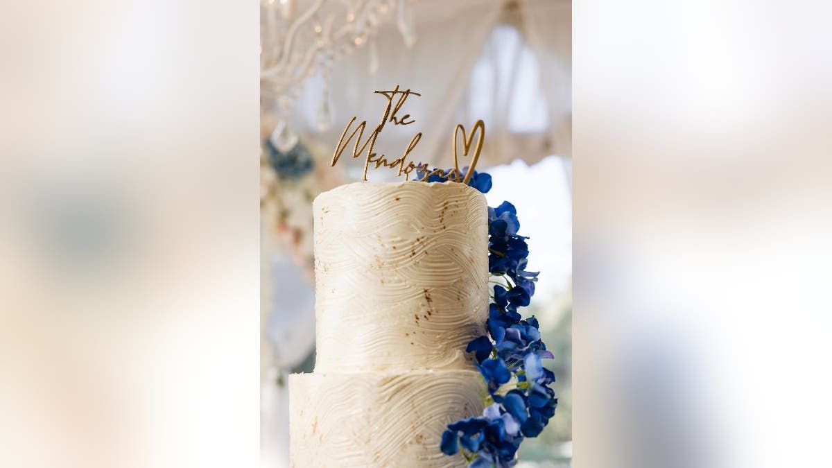 Top tier of a white wedding cake with a gold cake topper that says, 'The Mendozas.'