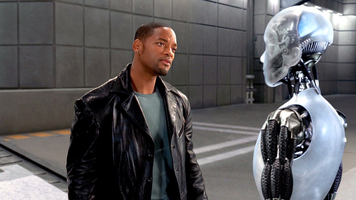 Will Smith in a black leather jacket as Del Spooner in "I, Robot" looking at a robot