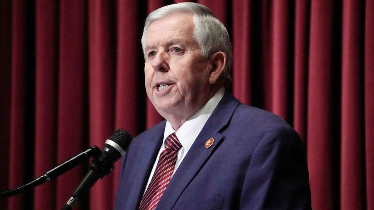 Mike Parson at microphone with curtain behind him