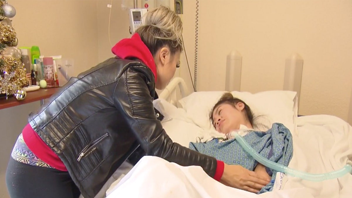 Lynn Fam stands over her daughter, who is in a hospital bed.