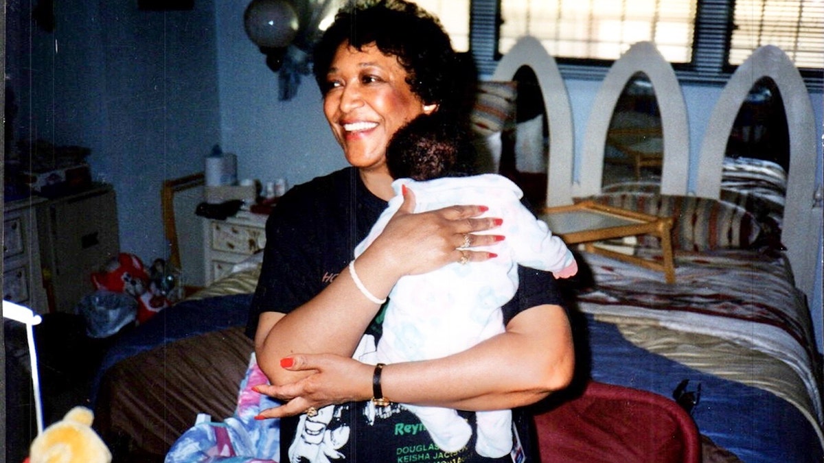 Minnie Smith smiling wearing a black shirt and holding an infant