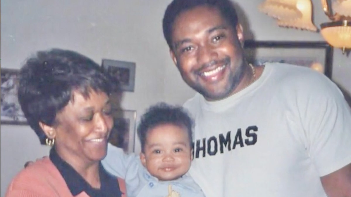 Minnie Smith is holding a smiling baby next to her smiling grandson wearing a grey sweatshirt