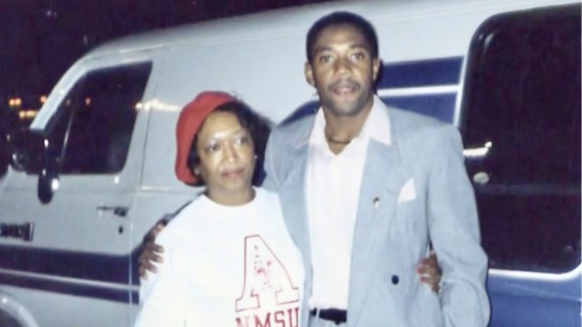 Minnie Smith wearing a white shirt and a red cap being held by her son