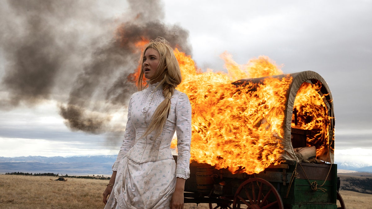 Isabel May wearing a prairie dress next to a fire