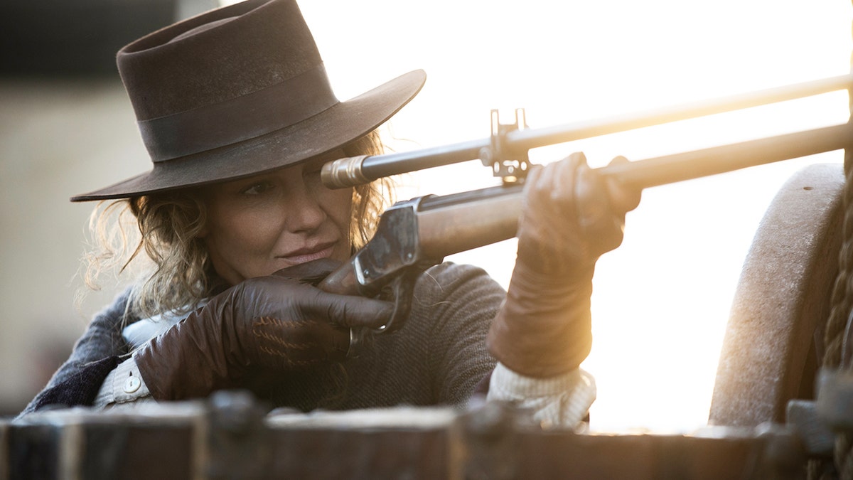 Faith Hill shooting a gun while wearing a cowboy hat.