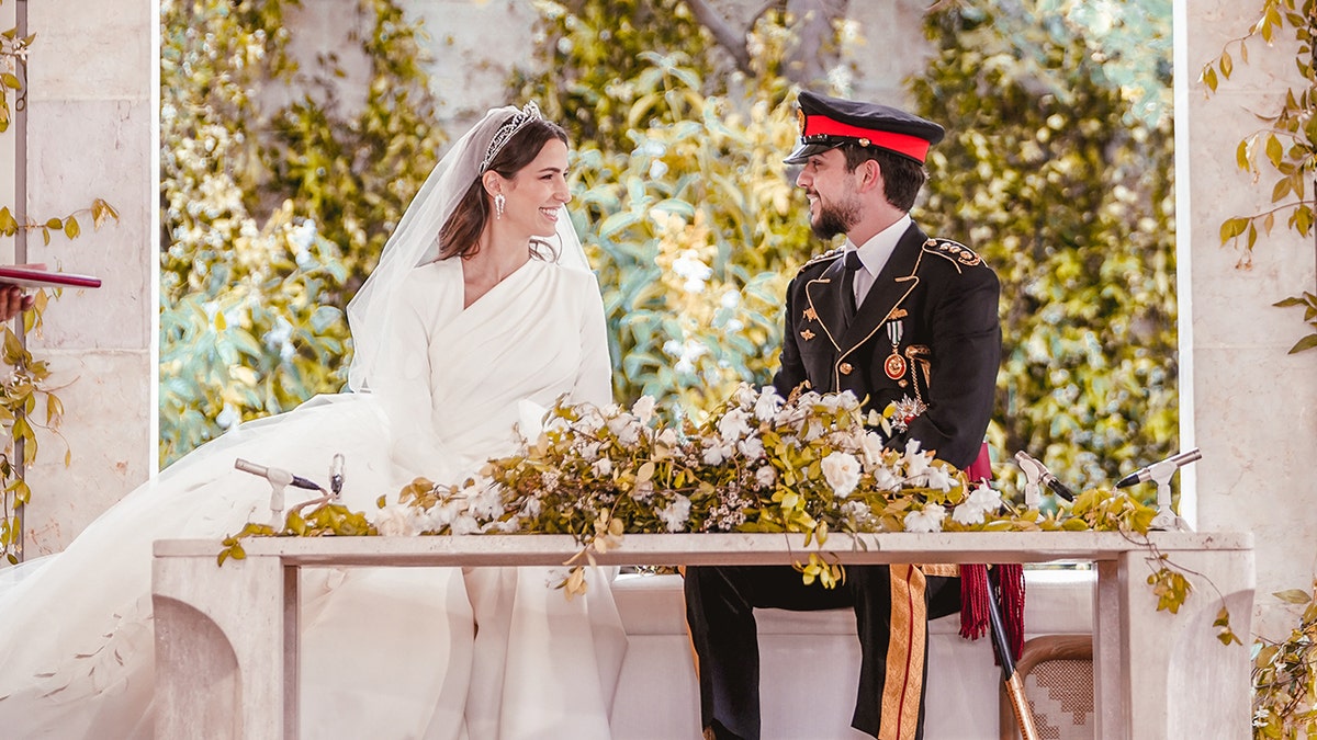 The royal bride and groom sitting together in front of a table with flowers
