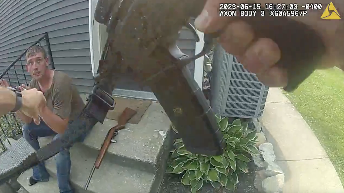 Ohio dad Chad Doerman sitting on stoop with rifle at his side as a responding officer approaches gun drawn