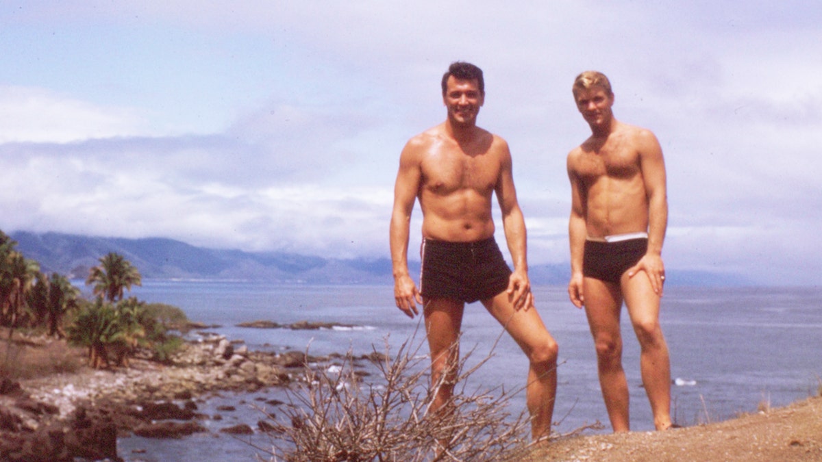 Rock Hudson on the beach with a male friend as they are both shirtless