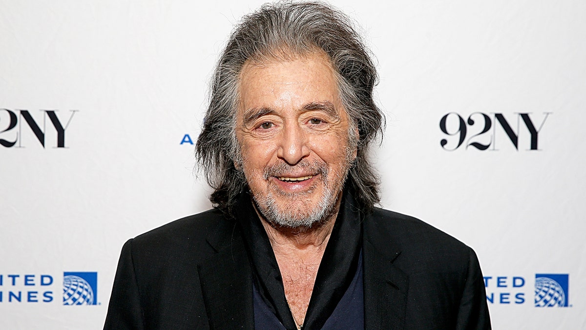 Al Pacino in a black suit jacket smiles for the camera on the carpet