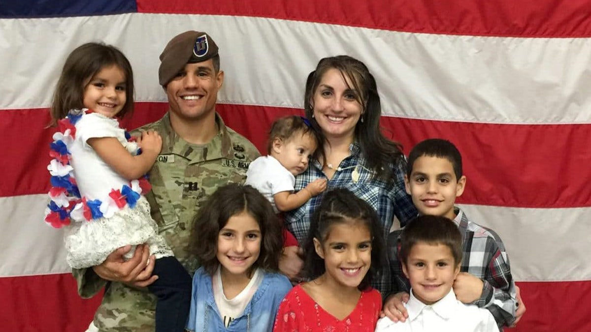 Army Capt. Gilberto De Leon stands in front of an American flag with his wife and children