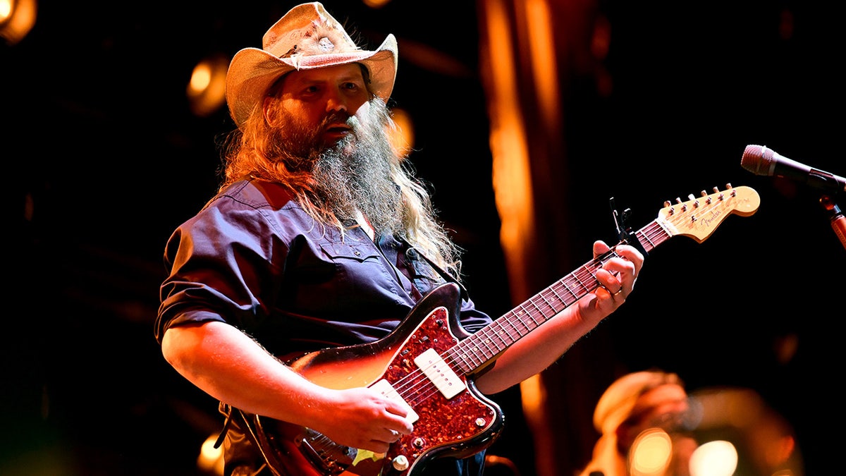 Chris Stapleton strums a guitar while on stage performing