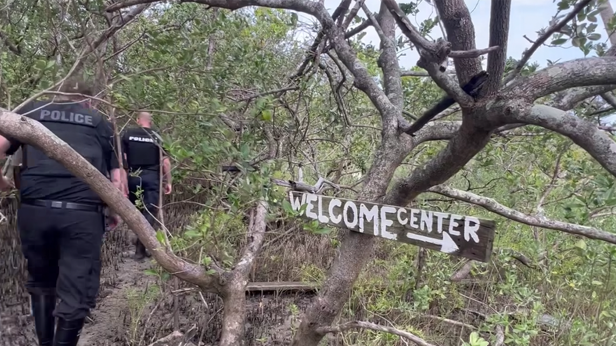 police walk by "welcome center" sign on squatter island