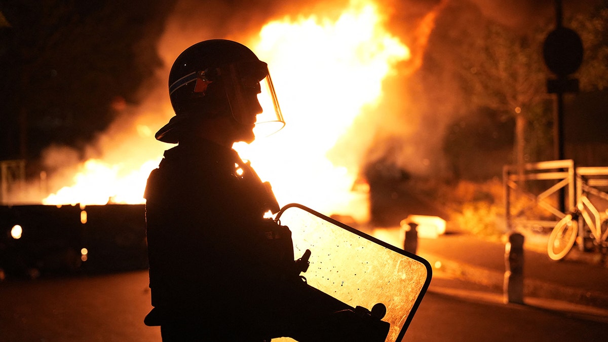 A firefighter looks on as vehicles burn following riots in Nanterre, west of Paris