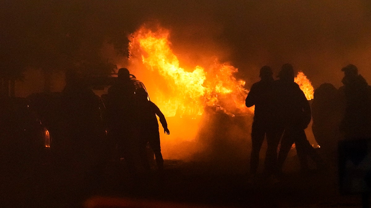 French rioters and police are hidden in shadow as a fire burns in the background during riots in Nanterre