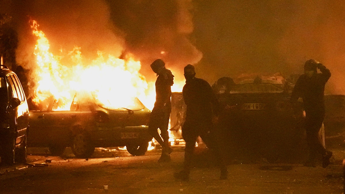 Rioters stand in front of burning vehicles during anti-police protests in France