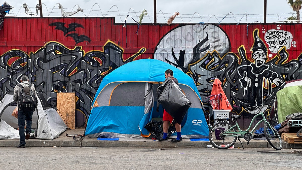 Two people walk in front of tents lining a San Diego street in the spring of 2023