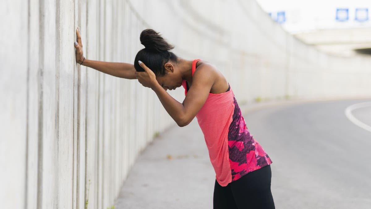 Woman holds onto concrete wall and appears to be dizzy.